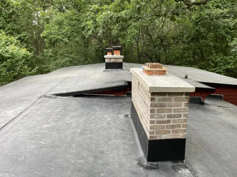 Flat roof with two brick chimneys surrounded by lush greenery.