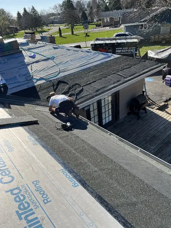 Roofer installing shingles on a residential roof under clear skies.